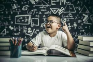 Happy boy wearing glasses studies math, surrounded by books and pencils.