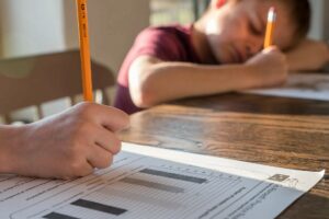 Two children working on worksheets at a table, one child appears to be sleeping. Handwriting and learning.